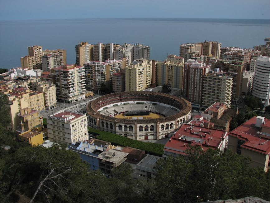 Aerial capture of Malaga's bullring surrounded by modern buildings and Mediterranean Sea.